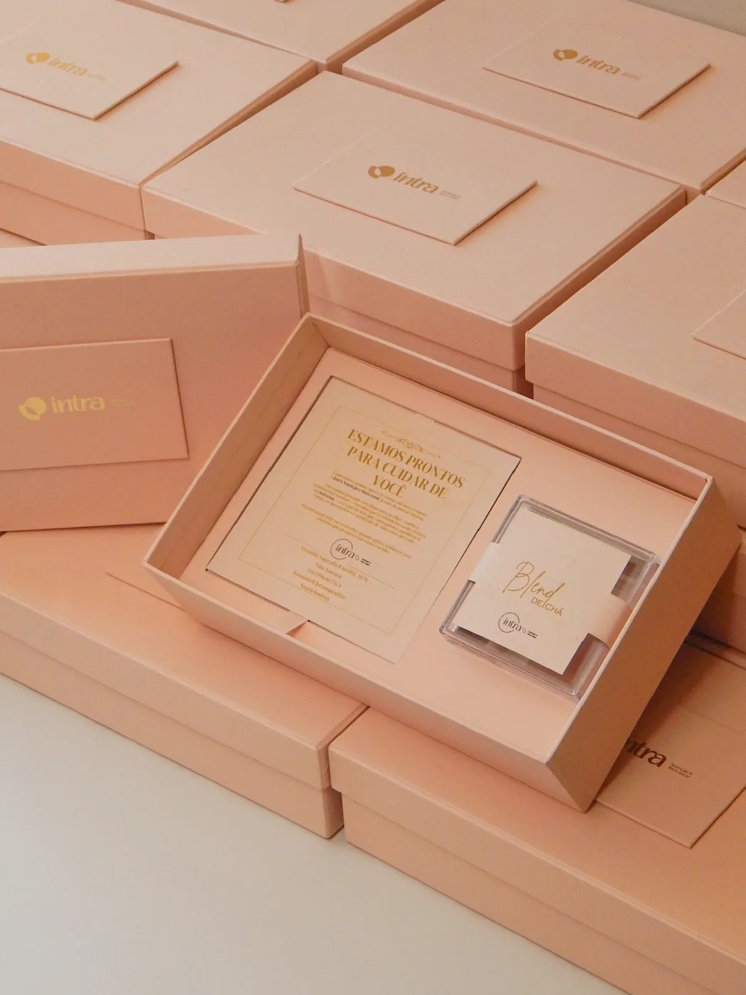 Caixas rosé abertas, com cartão impresso em dourado e o blend de chá no encaixe